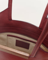 Interior view of a small garden tote bag in burgundy leather with walnut wood accents and a zippered pocket.