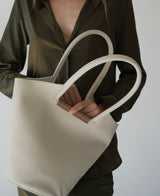 Small garden tote bag in cream held by a person wearing an olive shirt, featuring distinctive walnut wood detailing.